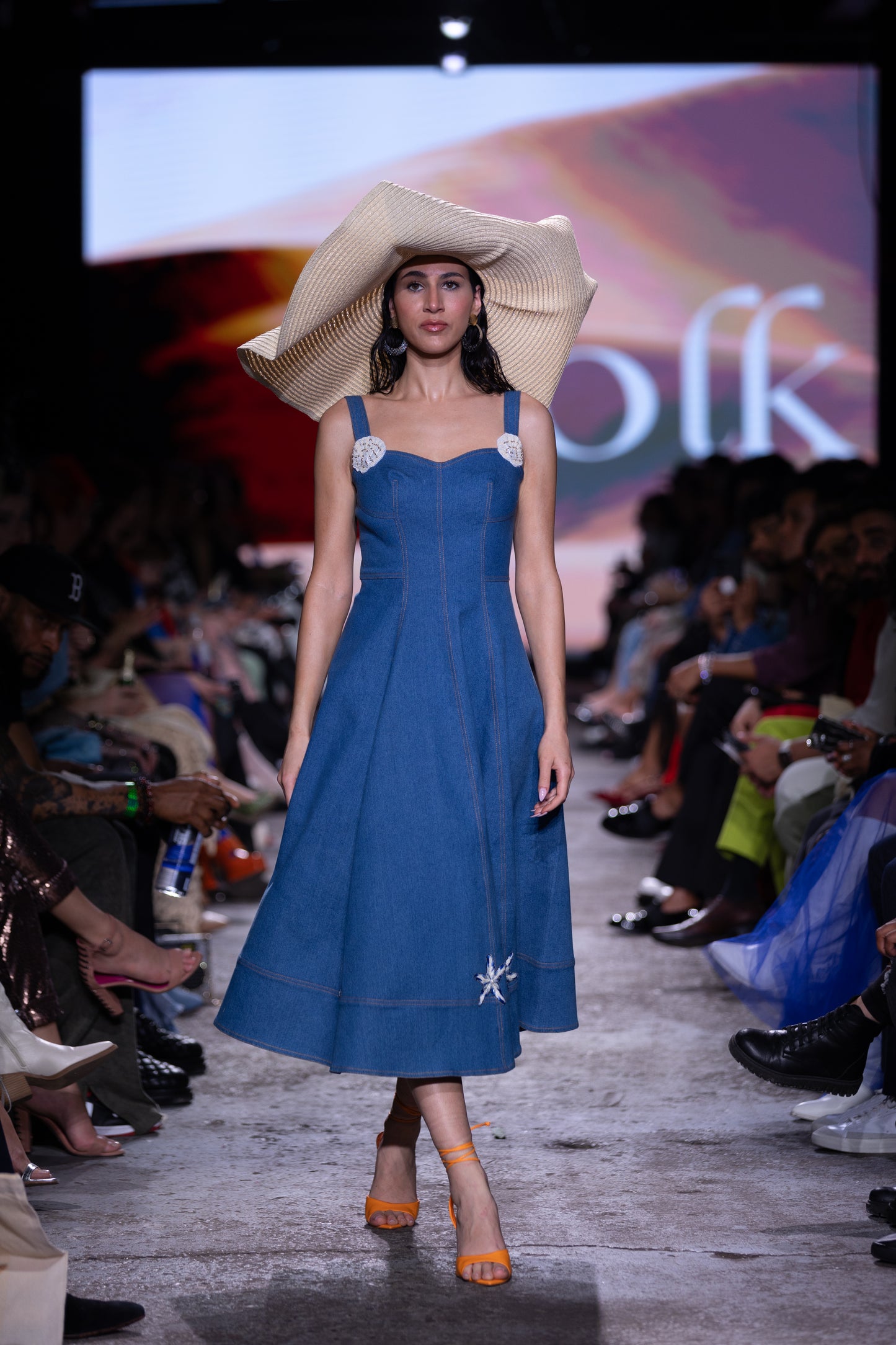 Model wearing a blue dress with white floral details on a fashion show runway.