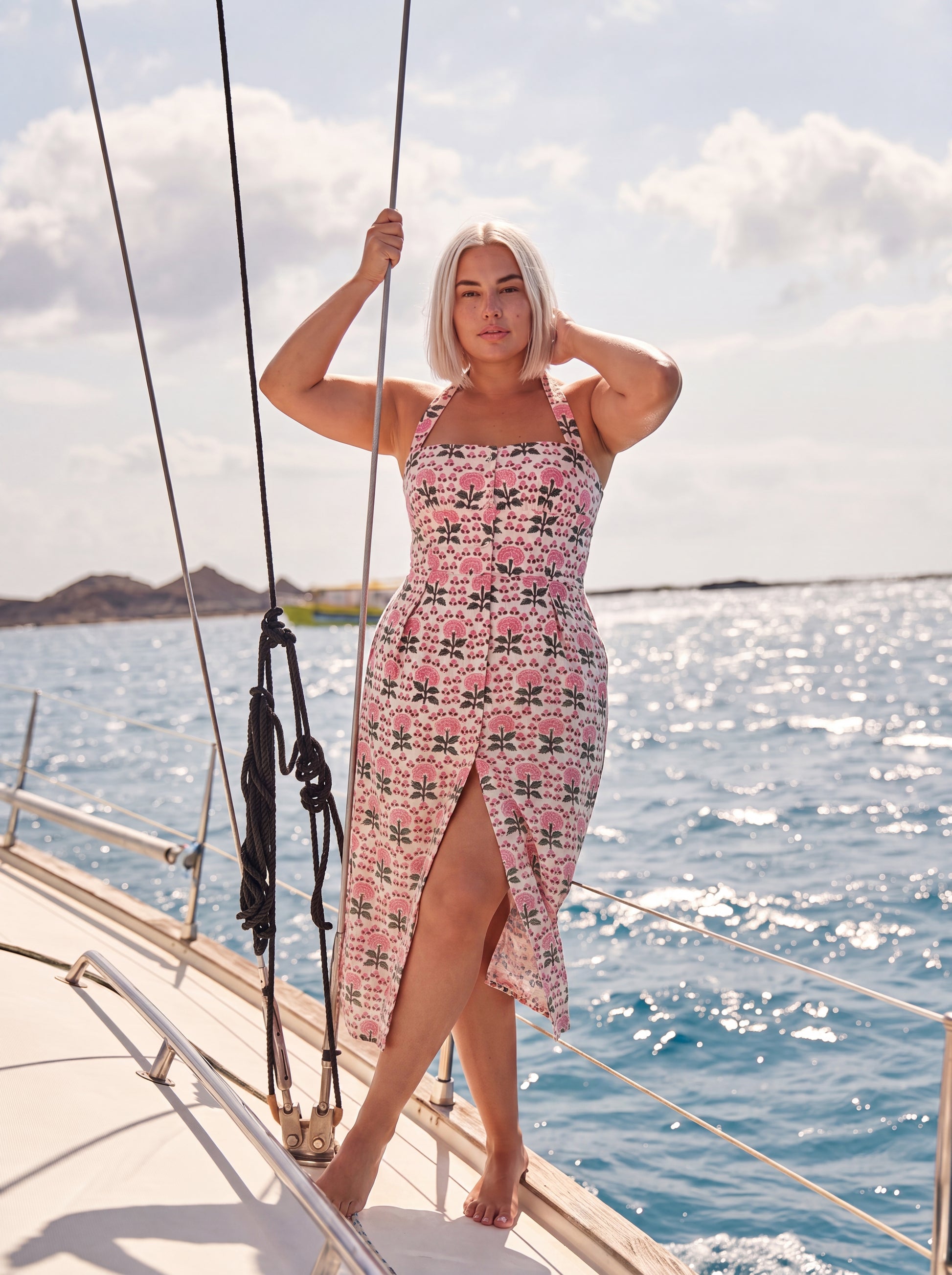 A woman standing on a sail boat wearing Pink Floral Halter Midi Dress