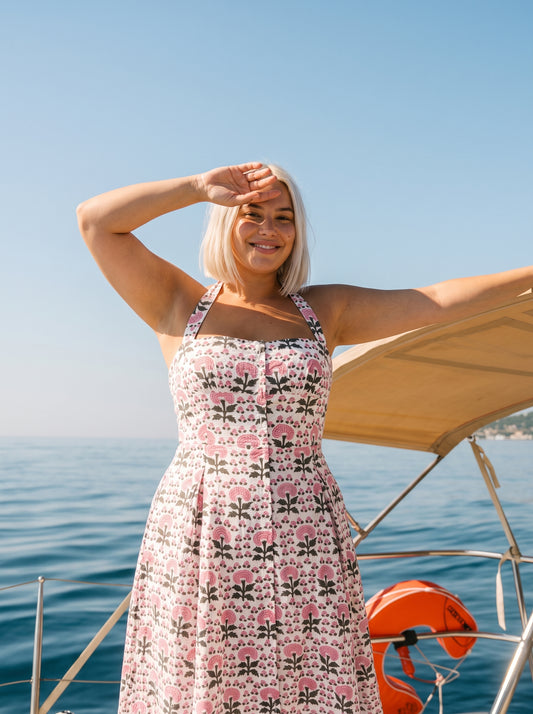 Woman wearing a pink floral halter midi dress with a fitted bodice, flowing skirt, and vintage-inspired floral print on a sailboat by the ocean.
